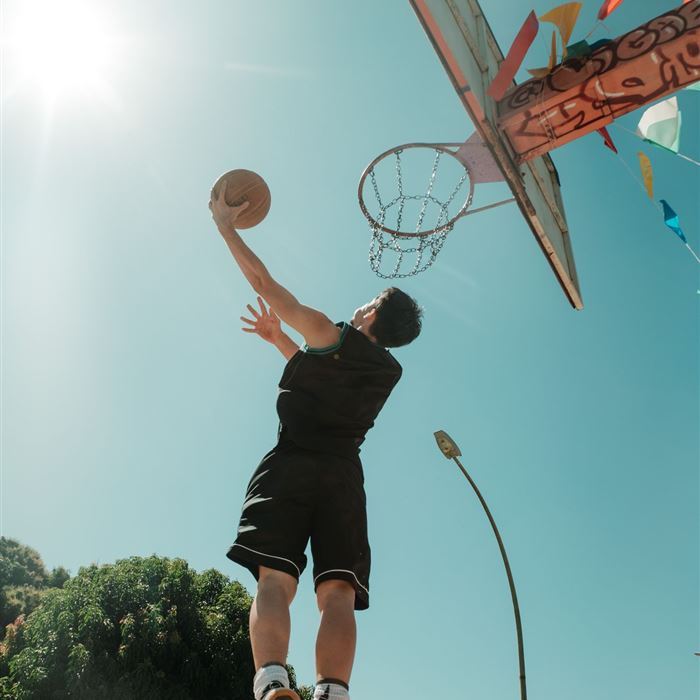 Player jumping with the ball toward an outdoor hoop under a blue sky