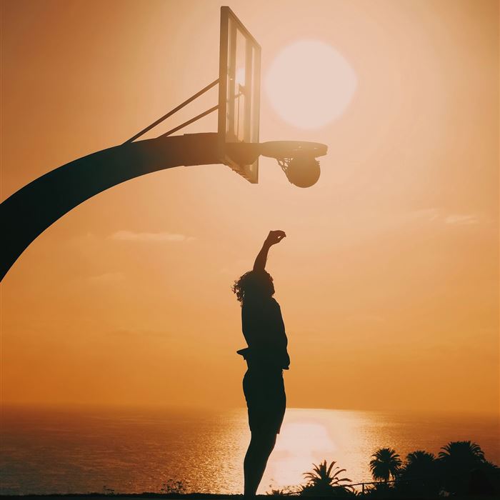 Silhouette of a player jumping toward a basketball hoop at sunset